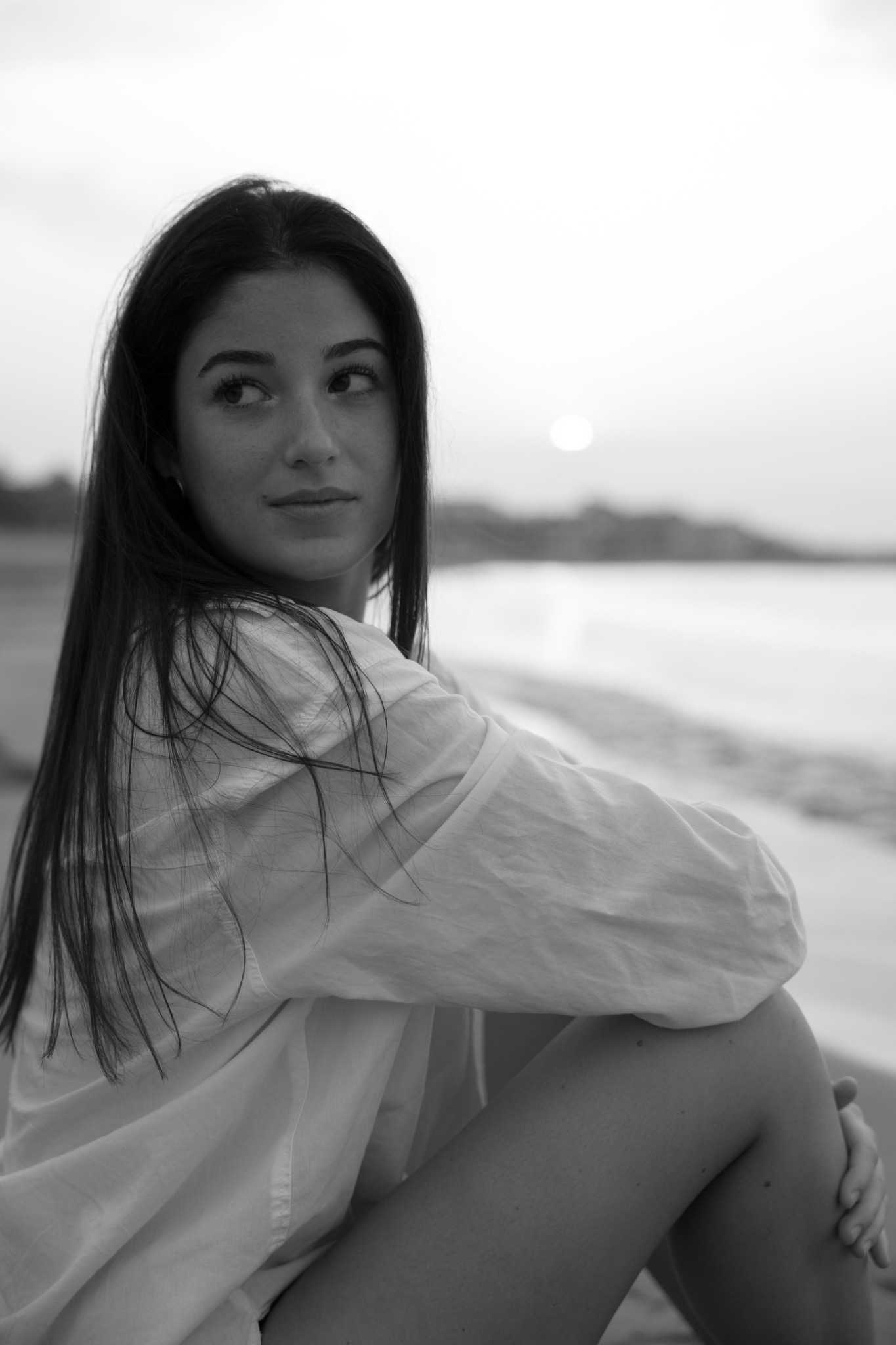 Judith en blanco y negro junto al mar, abrazándose las rodillas